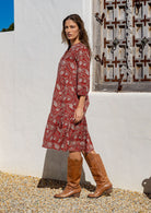 Model stands side on in cotton over the knee length relaxed fit dress with 3/4 sleeves, paired with brown boots. 