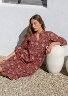 Woman in a red floral dress sitting against a white wall.