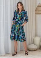 Woman poses in cotton tiered over the knee dress with 3/4 sleeves, buttoned bodice and V-neckline