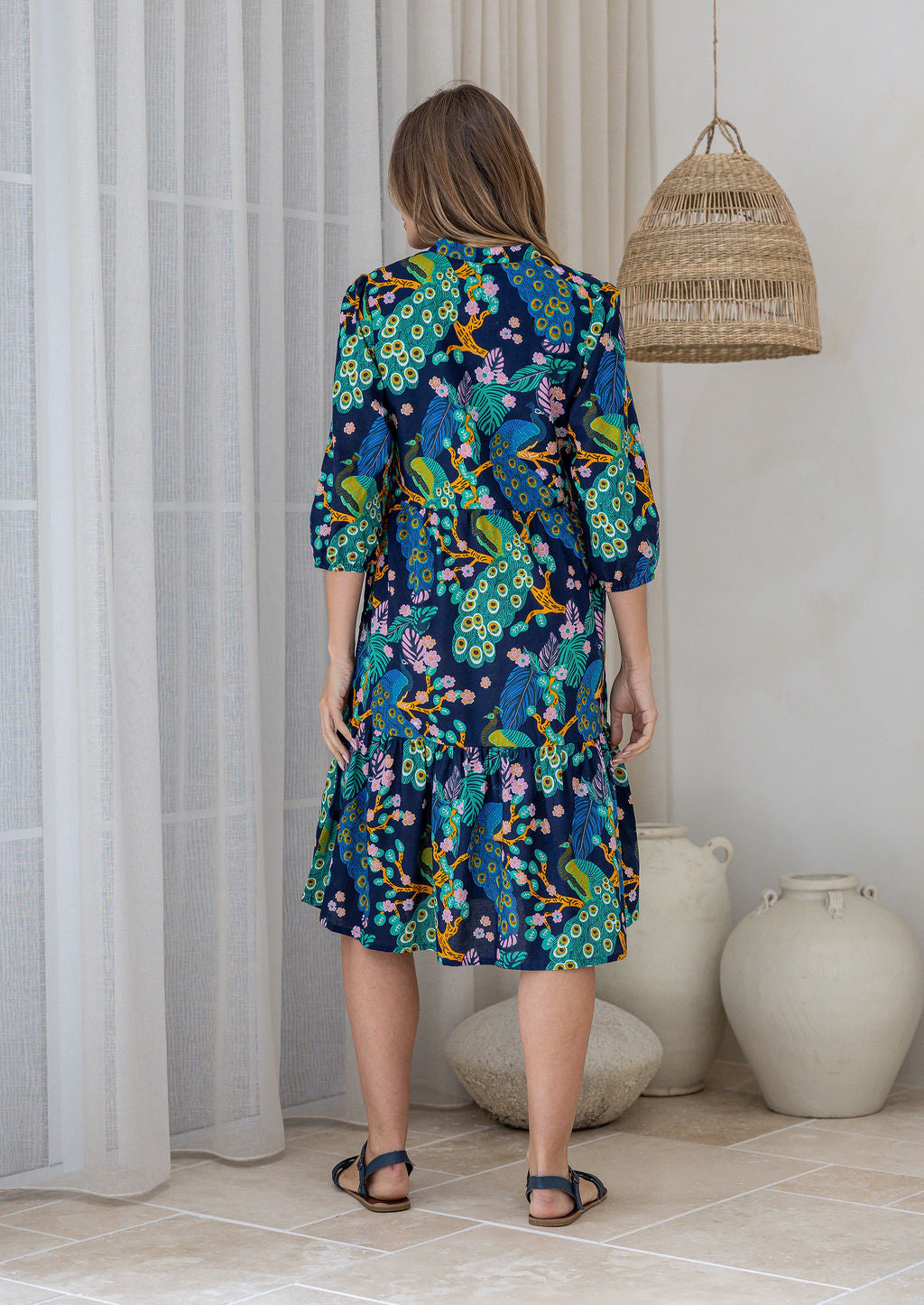 Model stands backwards on in cotton over the knee length relaxed fit dress with 3/4 sleeves, paired with sandals 