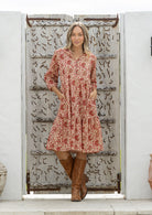 Woman wearing a red floral dress and brown boots standing in front of a decorative wooden door.