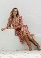 Woman in a floral dress and brown knee-high boots sitting on a white ledge.