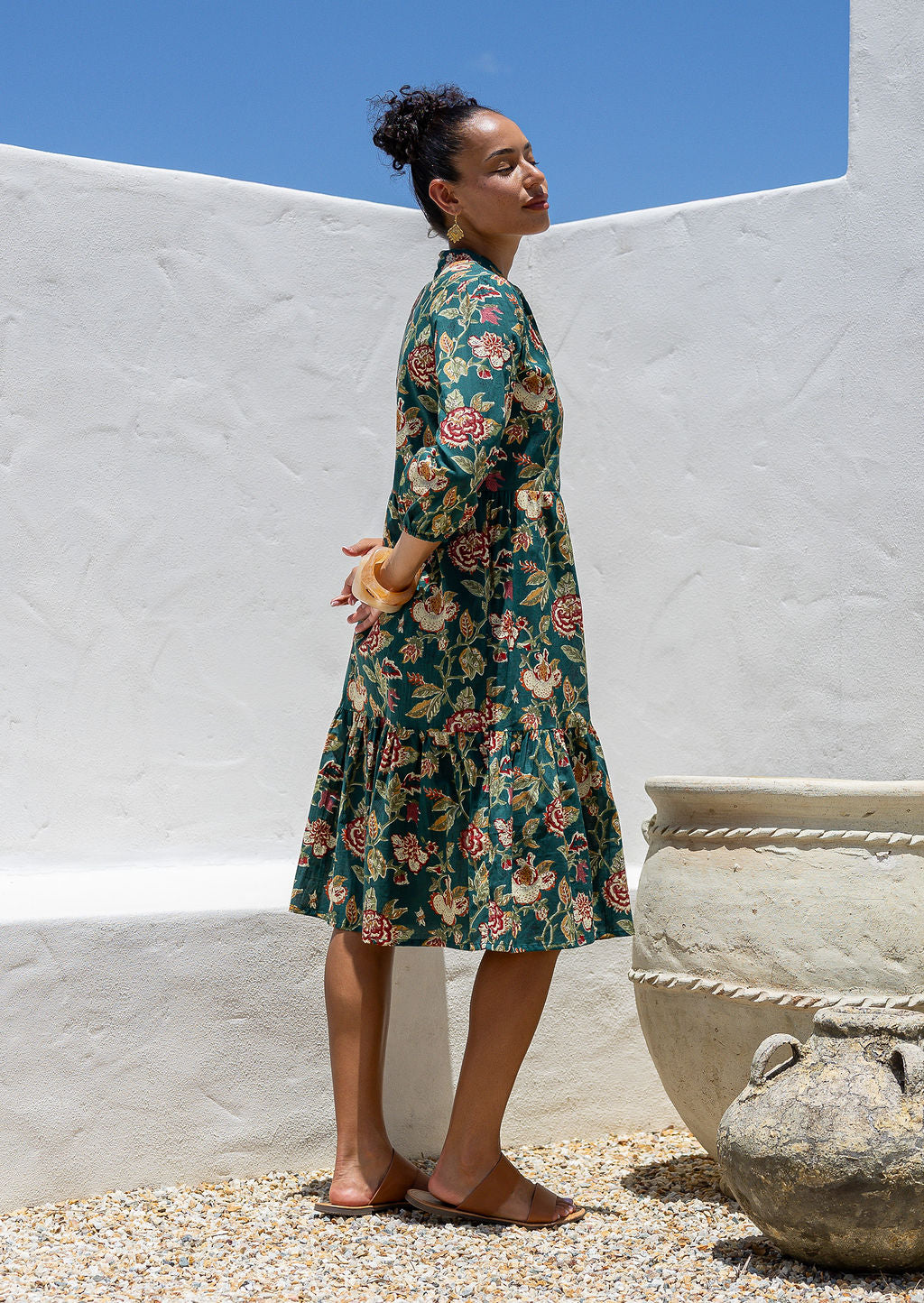 Model stands side on in cotton over the knee length relaxed fit dress with 3/4 sleeves, paired with tan sandals 