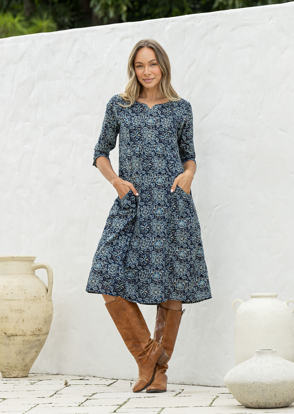 Woman wearing a 100% cotton navy blue based floral dress with sleeves and hands in pocket