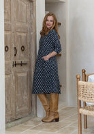 Woman stands sideways wearing a cotton navy blue based floral dress with sleeves.