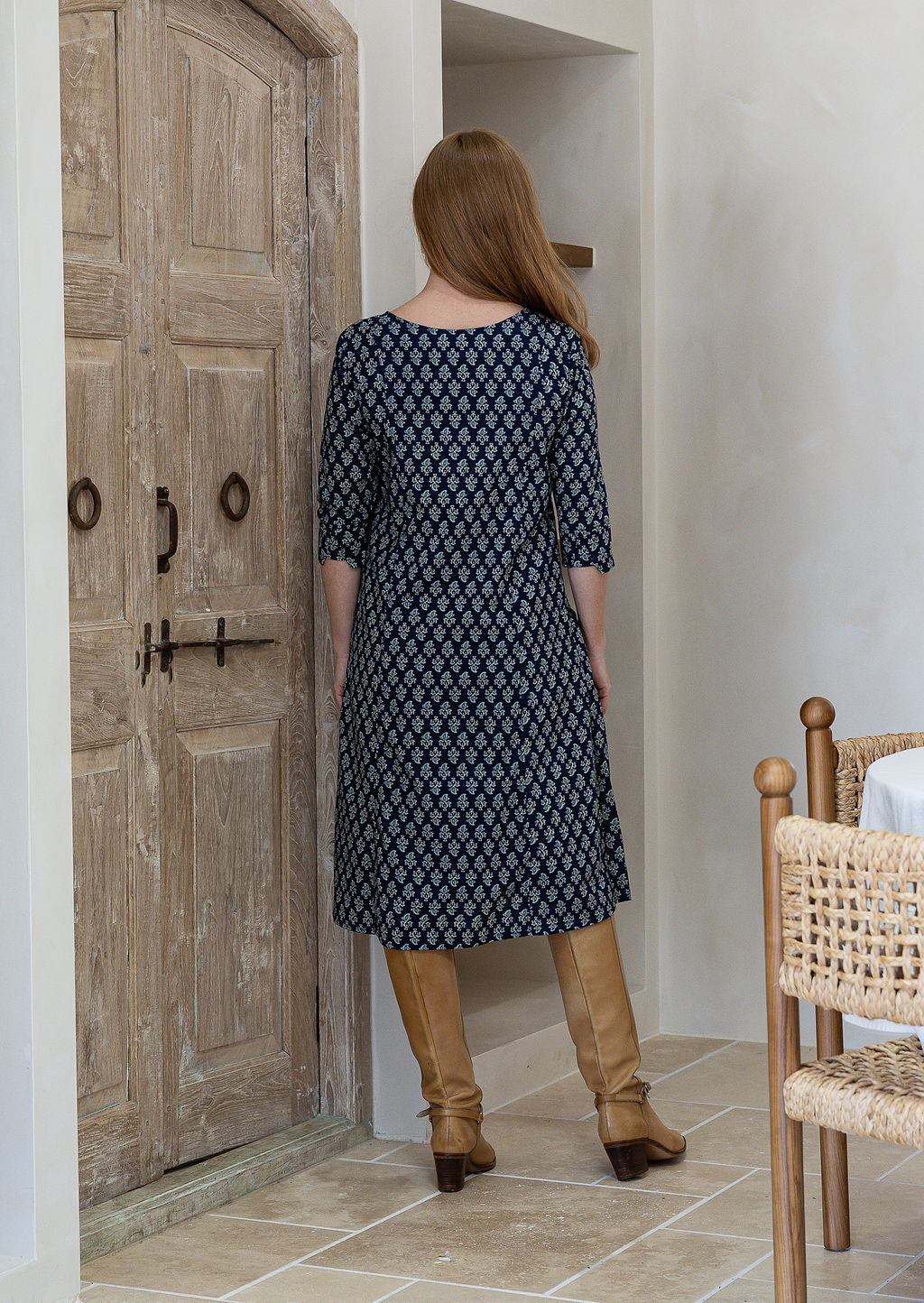 Woman stands backwards wearing a cotton navy blue based floral dress with sleeves