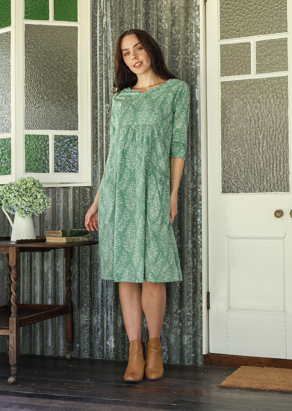 Woman poses in a 100% cotton sage green based floral dress with sleeves and  pockets