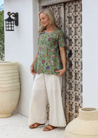 Woman wearing a relaxed fit 100% cotton top in moss green based floral print, paired with white cotton pants
