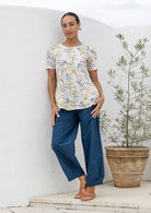Woman standing wearing a lightweight 100% cotton neutral floral print top with plain blue cotton pants