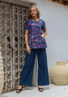 Woman standing with hand in top's pocket, wearing a lightweight 100% cotton blue floral print top with dark blue cotton pants