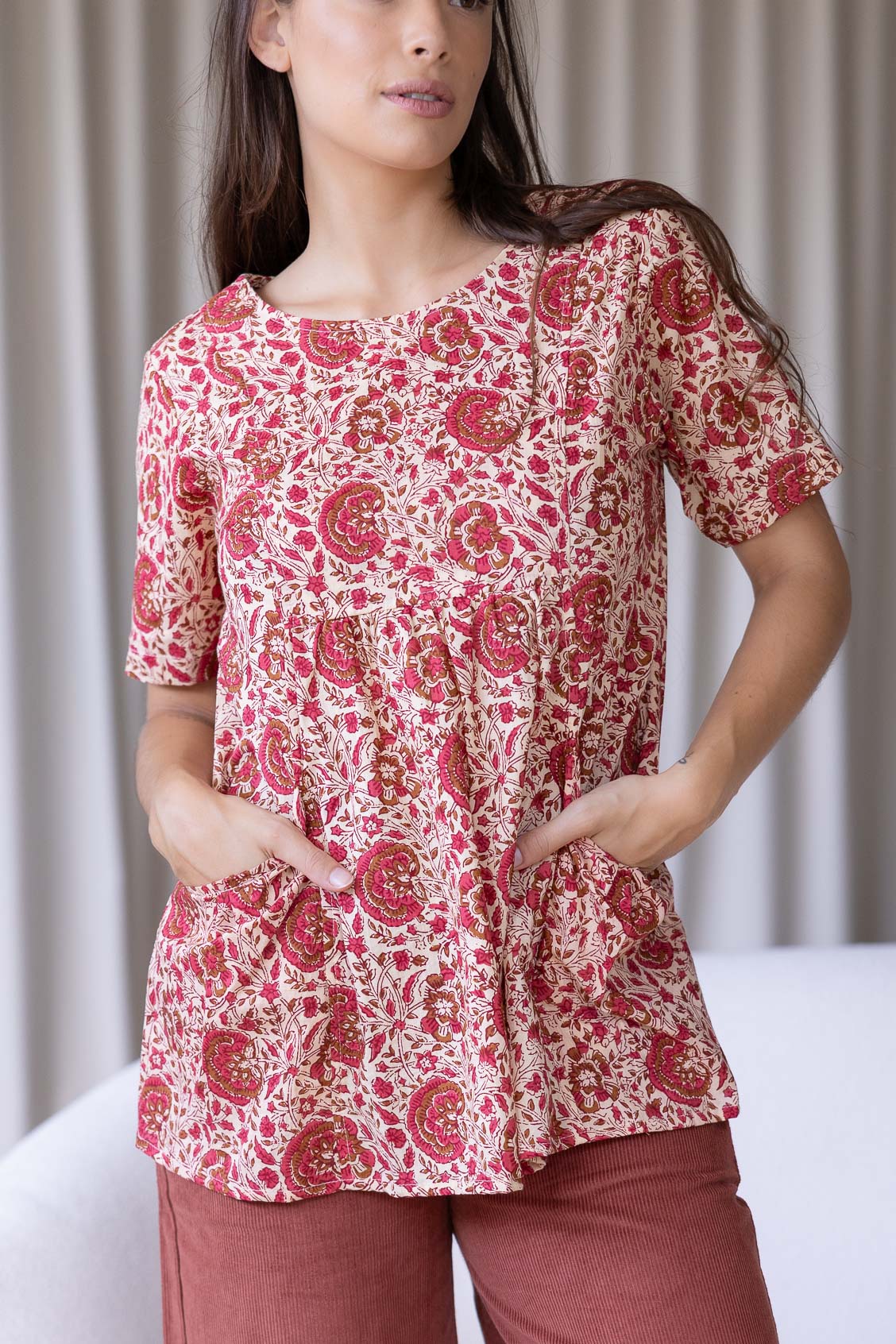 Woman wearing a gentle cream based floral print top with short sleeves, an empire waistline and deep pockets.