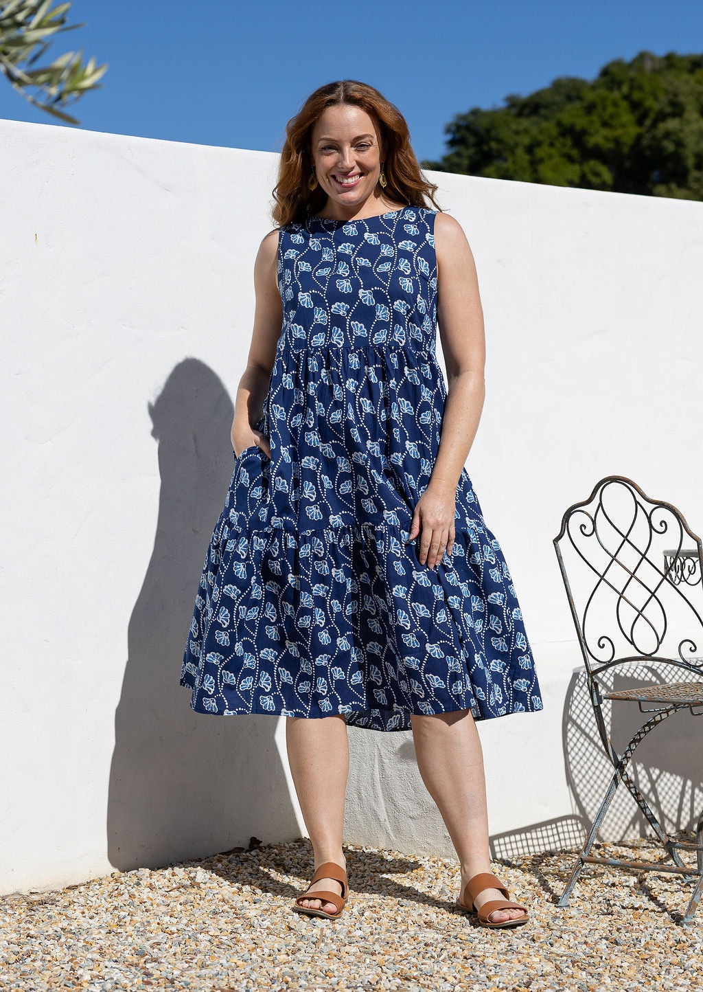 Woman wears a sleeveless, relaxed fit  floral cotton dress with tiered style, empire waist and pockets.