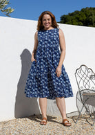 Woman wears a sleeveless, relaxed fit  floral cotton dress with tiered style, empire waist and pockets.