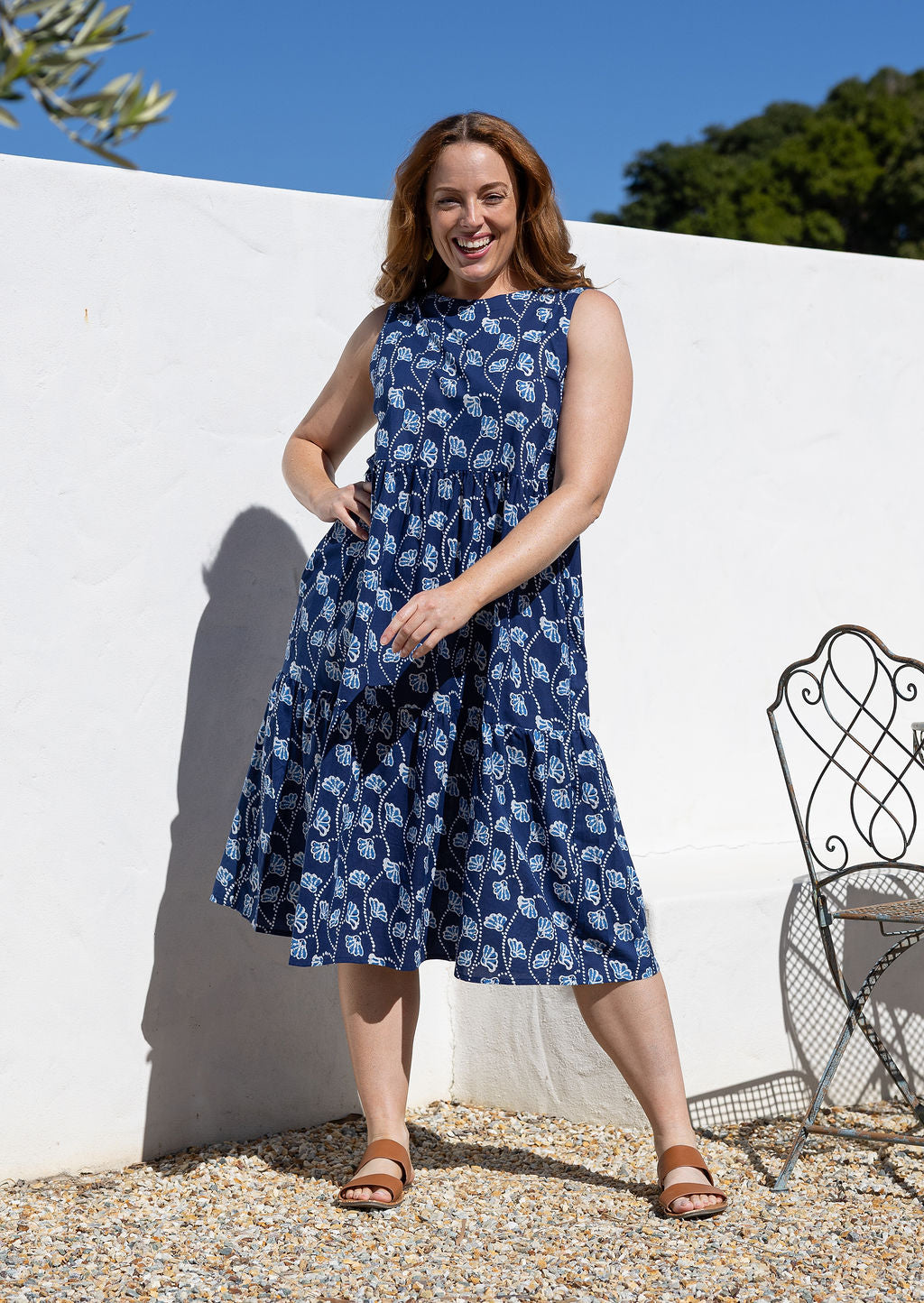 Woman wearing a tiered sleeveless sundress with pockets, high round neck and empire waist.