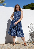 Woman wearing a tiered sleeveless sundress with pockets, high round neck and empire waist.