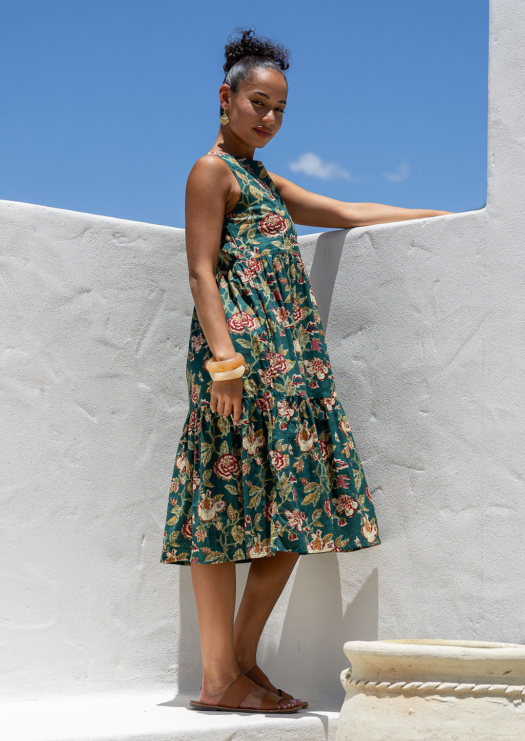 Woman wears a sleeveless, relaxed fit  floral cotton dress with tiered style, empire waist and pockets.