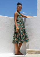 Woman wears a sleeveless, relaxed fit  floral cotton dress with tiered style, empire waist and pockets.