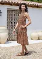 Model stands sideways in cotton sleeveless midi length dress in Indian floral print with hand in hidden side pocket