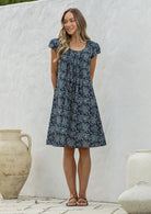 Woman standing wearing a 100% cotton navy blue based floral dress with round neckline.