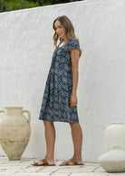Woman stands sideways wearing a 100% cotton navy blue based floral dress with round neckline.