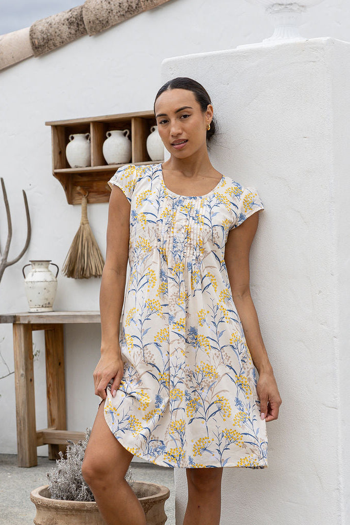 Woman wearing a neutral based floral cotton dress against a white background
