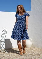 Woman poses in a 100% cotton navy blue based floral dress with round neckline and cap sleeves