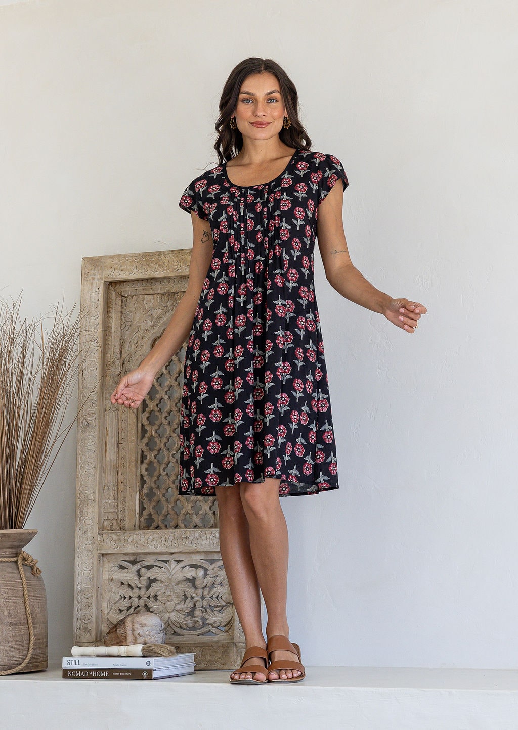 Woman poses in a 100% cotton black based floral dress with round neckline and cap sleeves