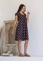 Woman stands sideways wearing a 100% cotton black based floral dress with round neckline.