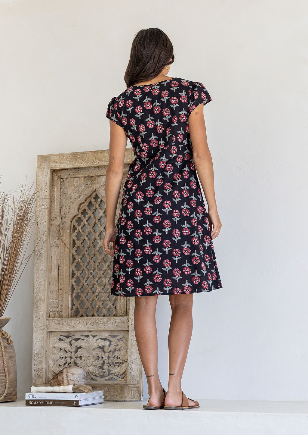 Woman stands backwards wearing a 100% cotton black based floral dress with round neckline.