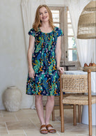 Woman wearing a 100% cotton navy based floral dress with round neckline and pin tucks across bust. 