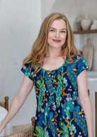 Woman standing wearing a 100% cotton navy based floral dress with round neckline.