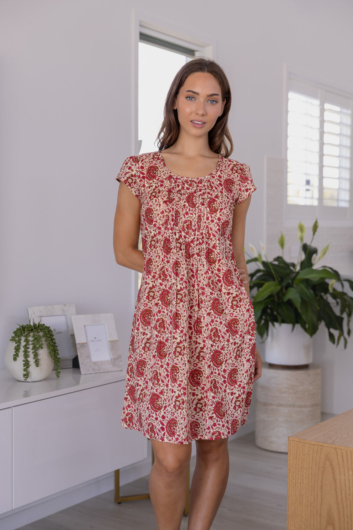 Woman wearing a 100% cotton gentle cream based floral dress with round neckline and cap sleeves.