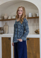 Woman in a blue floral top standing in a kitchen with wooden shelves and white cabinets.