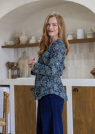 Woman standing sideways wearing a floral top and navy blue pants standing in a kitchen