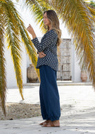 Woman standing sideways wearing a navy blue based floral top and navy plain pants standing outdoors.