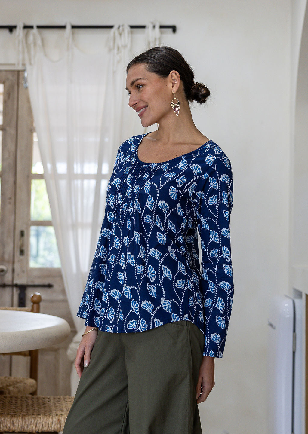 Woman standing sideways wearing a floral top and plain pants standing in an indoor setting