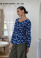Woman standing sideways wearing a floral top and plain pants standing in an indoor setting