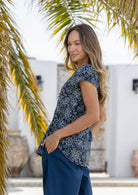 Woman stands sideways wearing  100% cotton top in navy blue based floral print with navy plain pants. 
