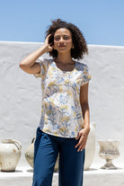 Woman wearing a neutral based floral print short sleeve top with scoop round neckline and pleated detail across the bodice
