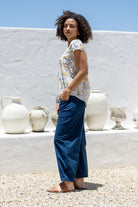 Woman standing sideways wears 100 percent cotton top with short cap sleeves and longer back hem.