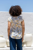 Woman standing backwards wears 100 percent cotton top with short cap sleeves and longer back hem.