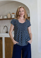 Woman wearing a navy blue based floral print short sleeve top with scoop round neckline and pleated detail across the bodice