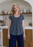 Woman wears navy blue based floral print 100% cotton cap sleeve top with pin tuck detail across the bust and a scoop neckline