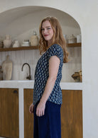 Woman stands sideways wearing  100% cotton top in navy blue based floral print with navy plain pants. 