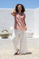 Woman wears rose pink based floral print 100% cotton cap sleeve top with pin tuck detail across the bust and a scoop neckline