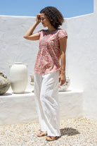 Woman standing sideways wears 100 percent cotton top with short cap sleeves and longer back hem.