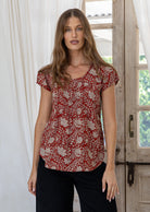 Woman wears red based floral print 100% cotton cap sleeve top with pin tuck detail across the bust and a scoop neckline