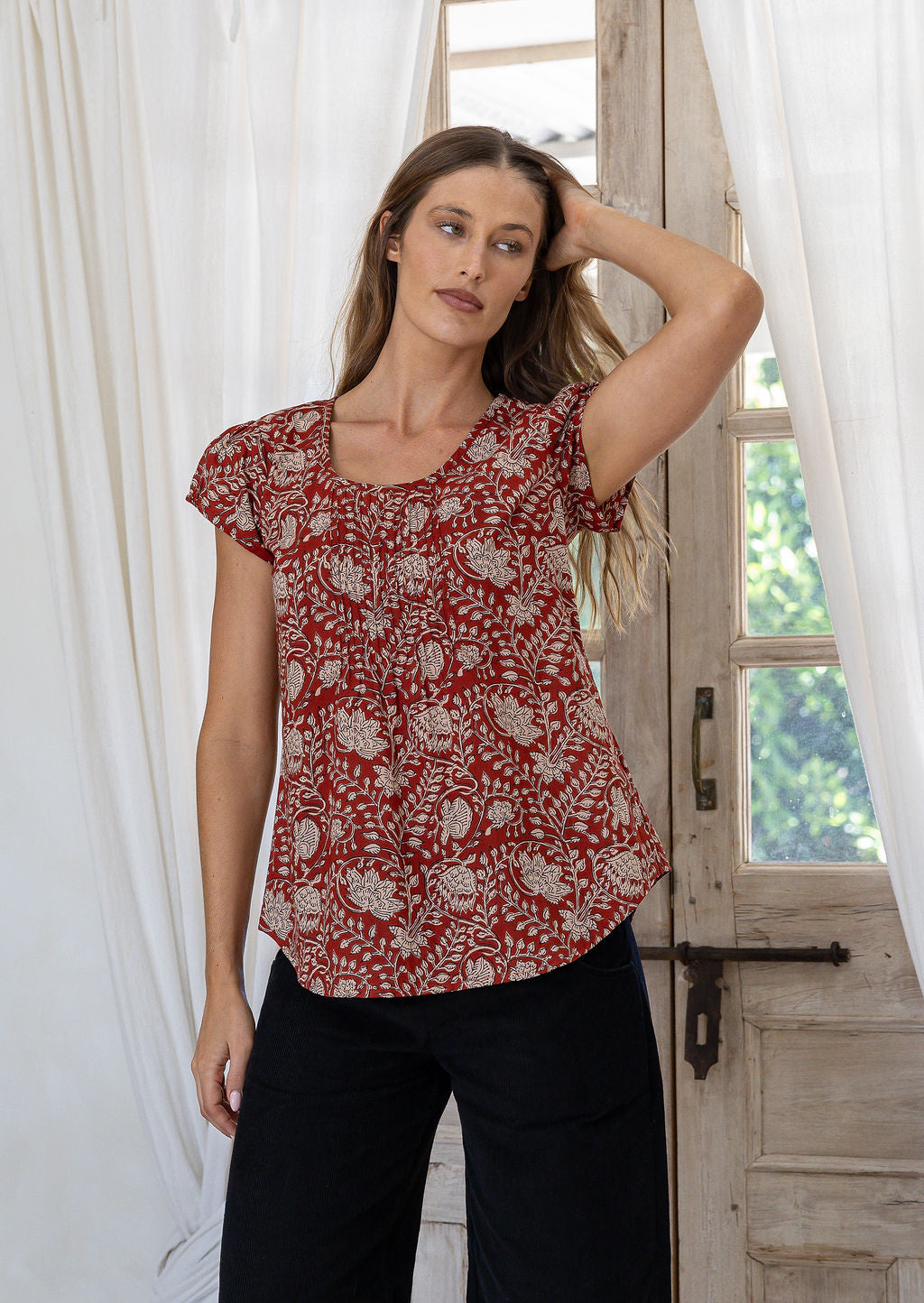 Woman wearing 100 percent cotton top with short cap sleeves and longer back hem.