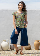 Woman wearing a moss green based floral  print short sleeve top with scoop round neckline and pleated detail across the bodice
