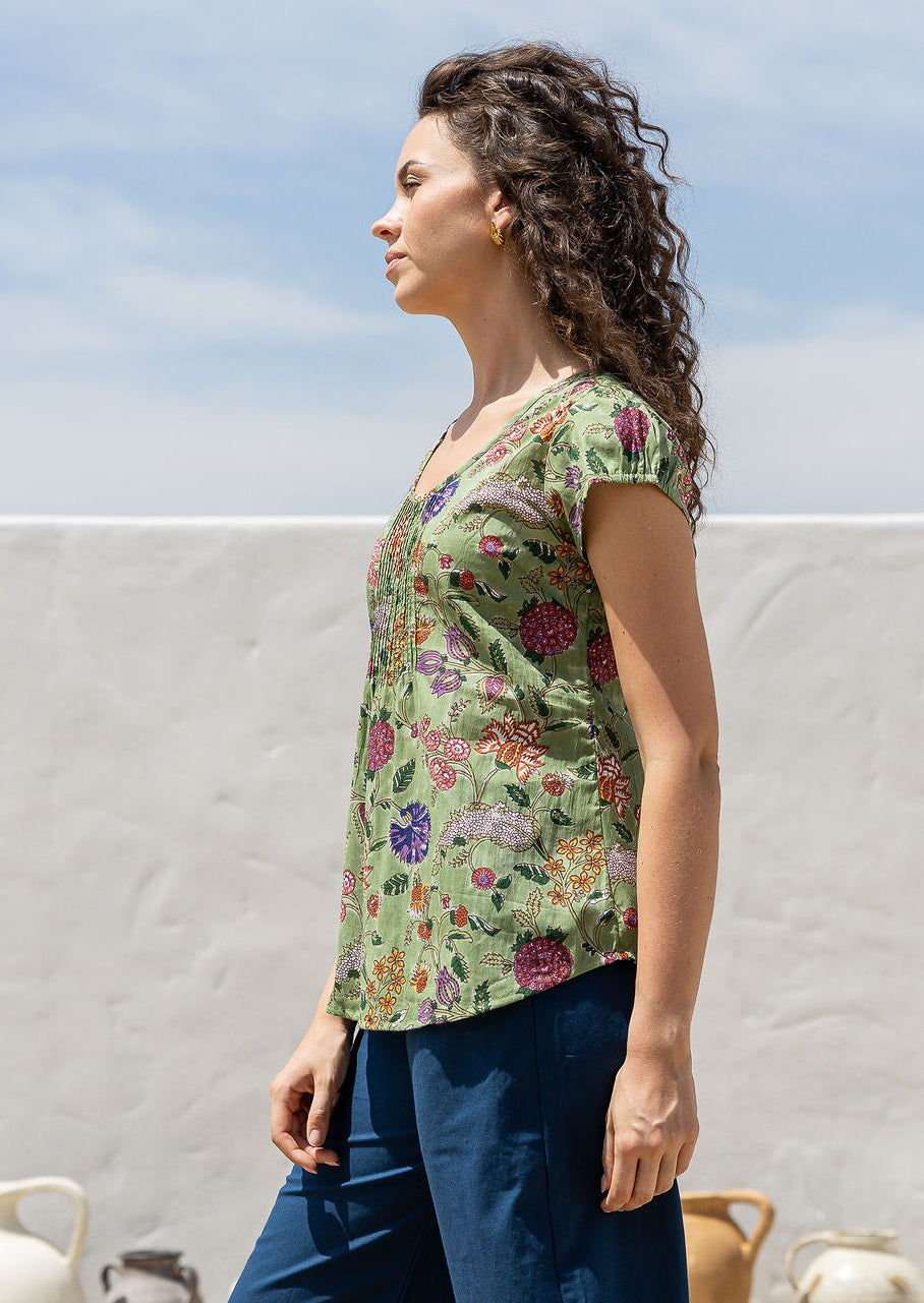Woman standing sideways wears 100 percent cotton top with short cap sleeves and longer back hem.